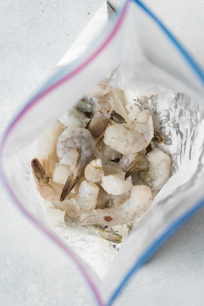 Raw shrimp being tossed in a gallon-size ziploc bag with cornstarch.