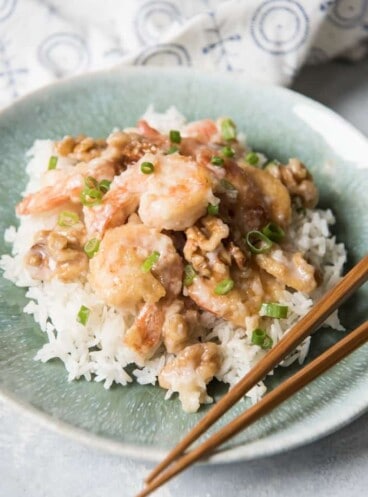 a blue plate with a pile of rice topped with honey walnut shrimp and chopsticks to the side