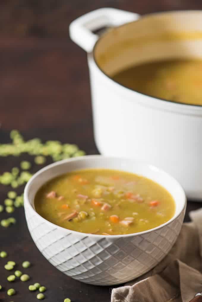 a white bowl of split pea soup next to a white pot