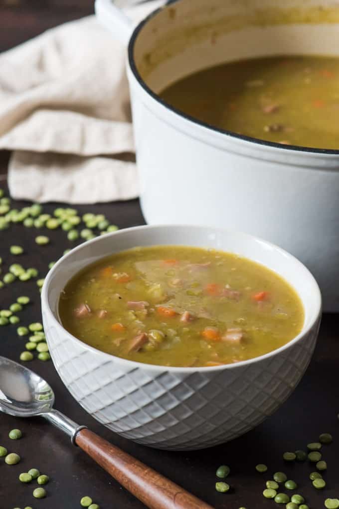 a white bowl of split pea soup next to a white pot of more soup