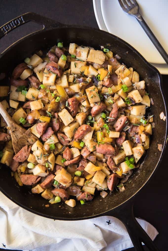 a cast iron skillet full of sweet apple hash with plates and a fork to the side