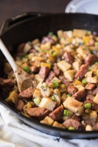 a wooden spoon in a skillet full of Sweet Potato Hash with Sausage & Apples