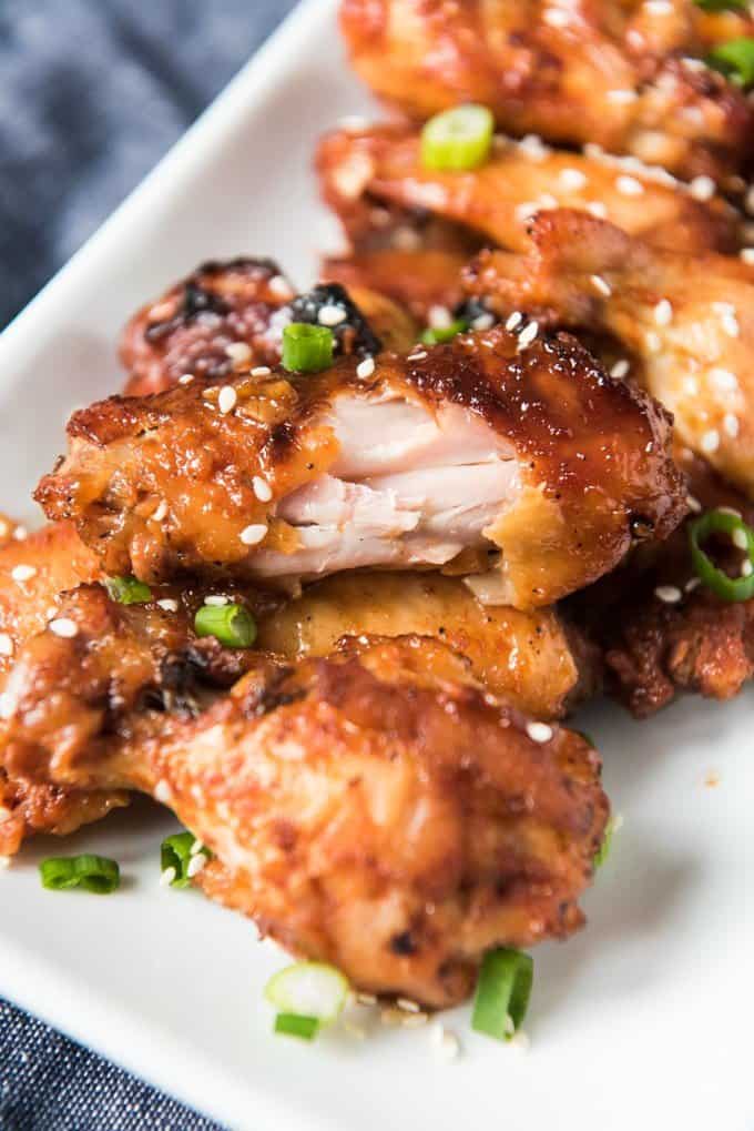 A plate of oven baked chicken wings made with a Korean BBQ sauce, with a bite already taken out of one of the crispy, sticky wings.