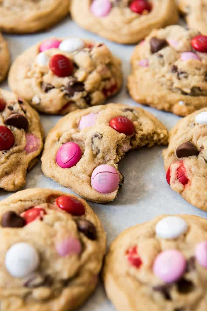 Soft, chewy chocolate chip M&M cookies arranged on a flat surface with one bite taken out of one of them.