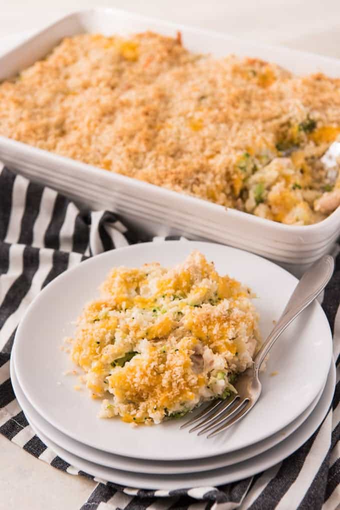 stacked white plates with chicken broccoli rice casserole and a fork in front of a baking dish of more casserole