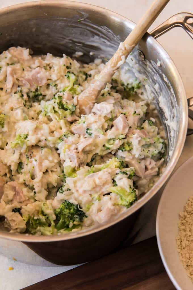 Chicken and rice in a pot being mixed together with broccoli and a creamy, cheesy sauce.