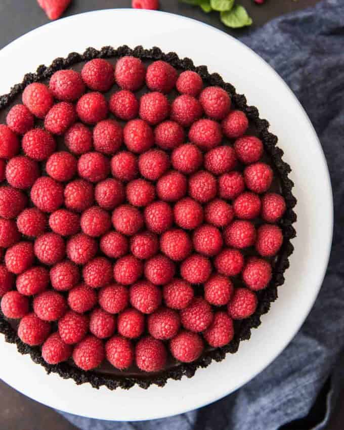 An aerial view of raspberry tart on white cake stand with fresh berries below.