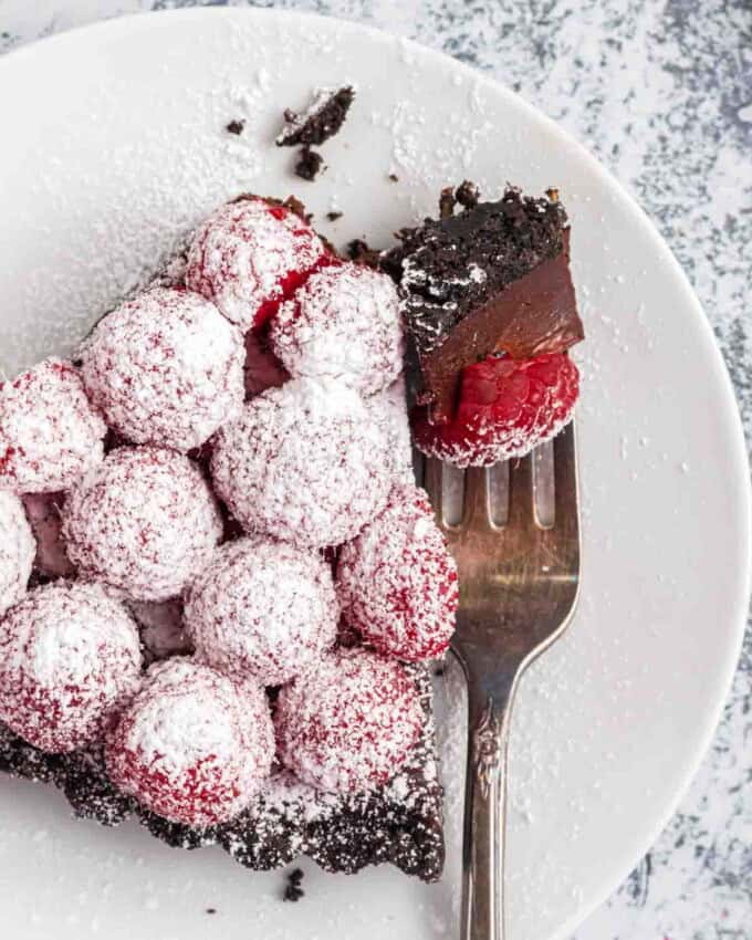 An overhead image of a slice of raspberry chocolate tart on a plate with a fork holding a bite of it.