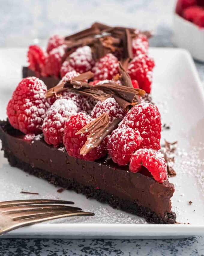 Two slices of raspberry chocolate tart with shaved chocolate and a dusting of powdered sugar on top.