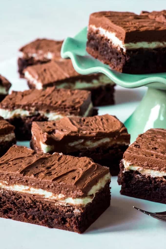 several pieces of frosted mint brownie around a cakeplate with a piece of brownie on top
