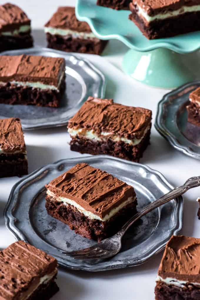 sliced servings of frosted mint brownies resting on and off plates or a cakestand