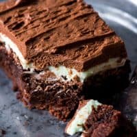 One fudgy frosted chocolate mint brownie with layers of chocolate and mint frosting on a plate with a bite taken out of it.