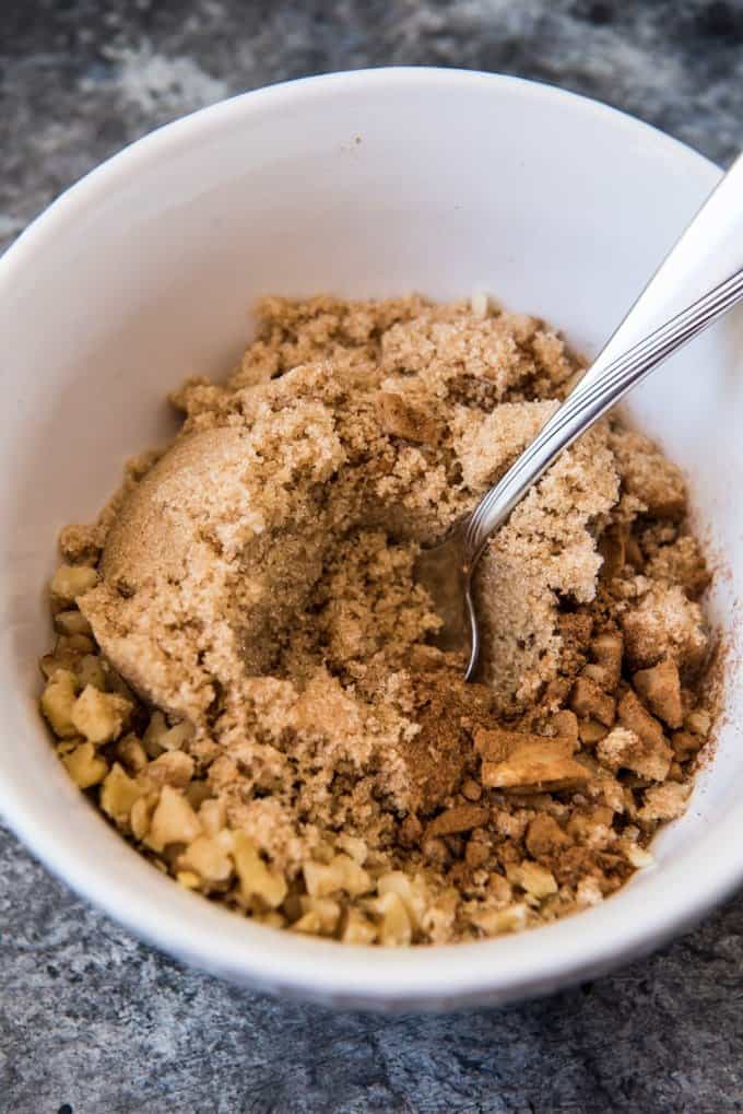 Brown sugar, cinnamon and chopped walnuts in a white bowl with a spoon to mix them together for a sweet korean pancake filling.