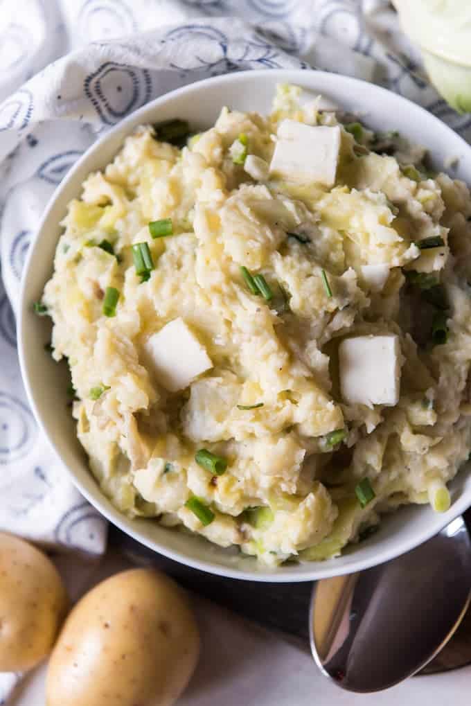 irish colcannon with 3 small squares of butter resting in a white bowl next to potatoes and a spoon