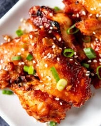 A white rectangular serving plate full of Oven Baked Korean BBQ Chicken Wings that are sweet, savory & spicy, thanks to a Korean red chile pepper paste called gochujang that adds fantastic flavor to this Asian-inspired Korean barbecue sauce. Garnished with sesame seeds and green onions.