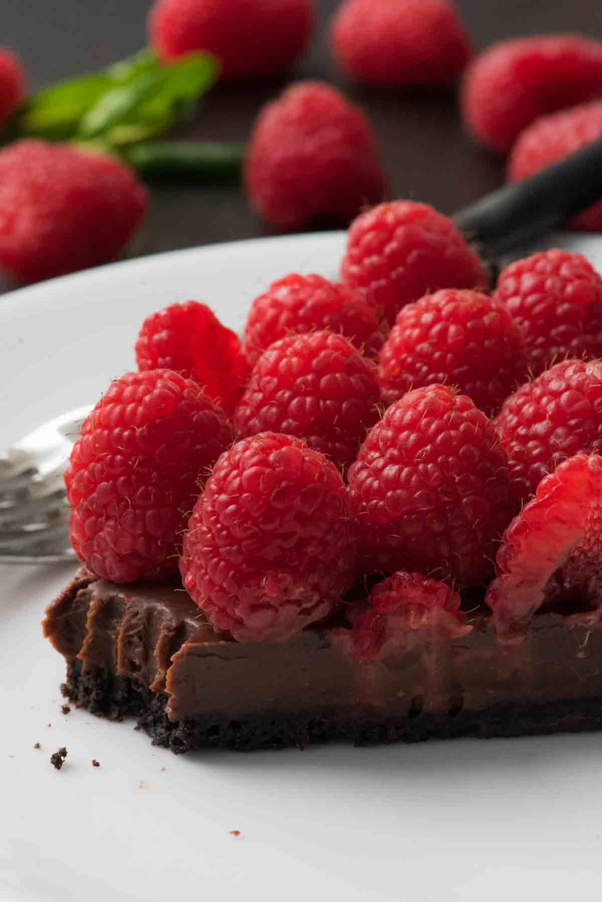 One slice of fresh raspberry chocolate tart with a bite taken out of it.