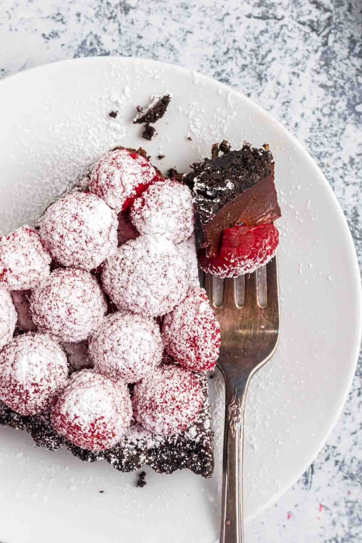 An overhead image of a slice of raspberry chocolate tart on a plate with a fork holding a bite of it.