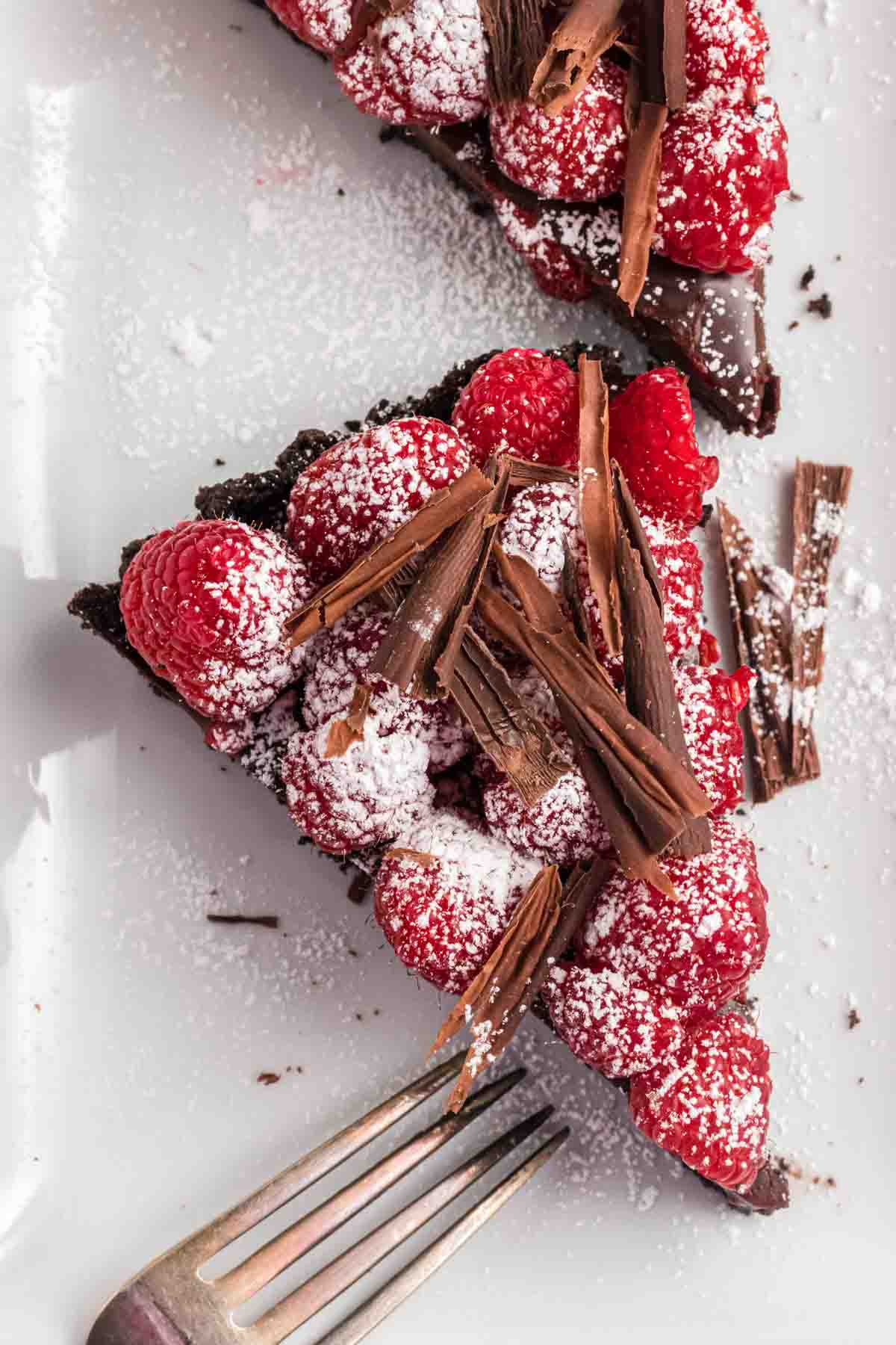 Slice of chocolate tart with raspberries on a white plate with a fork.