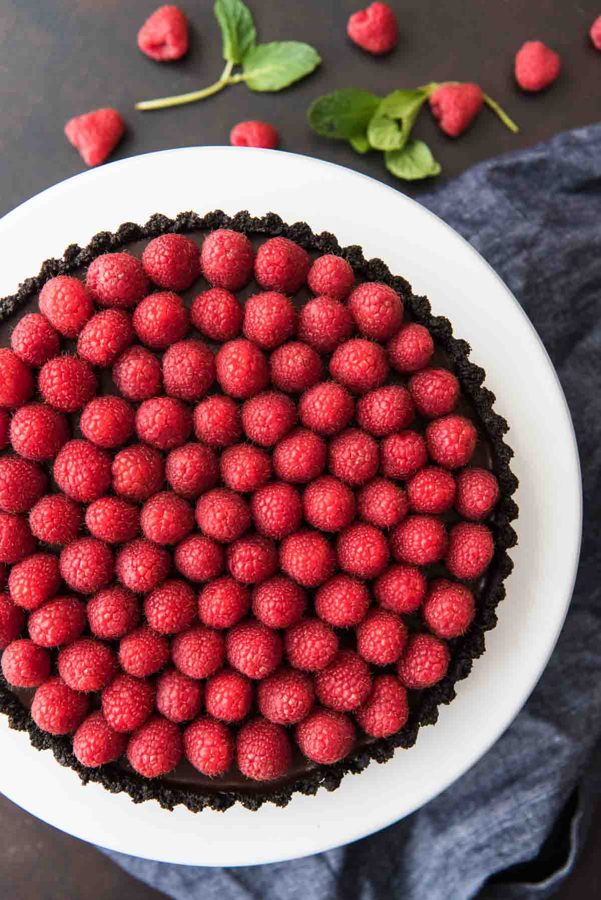 An aerial view of raspberry tart on white cake stand with fresh berries below.