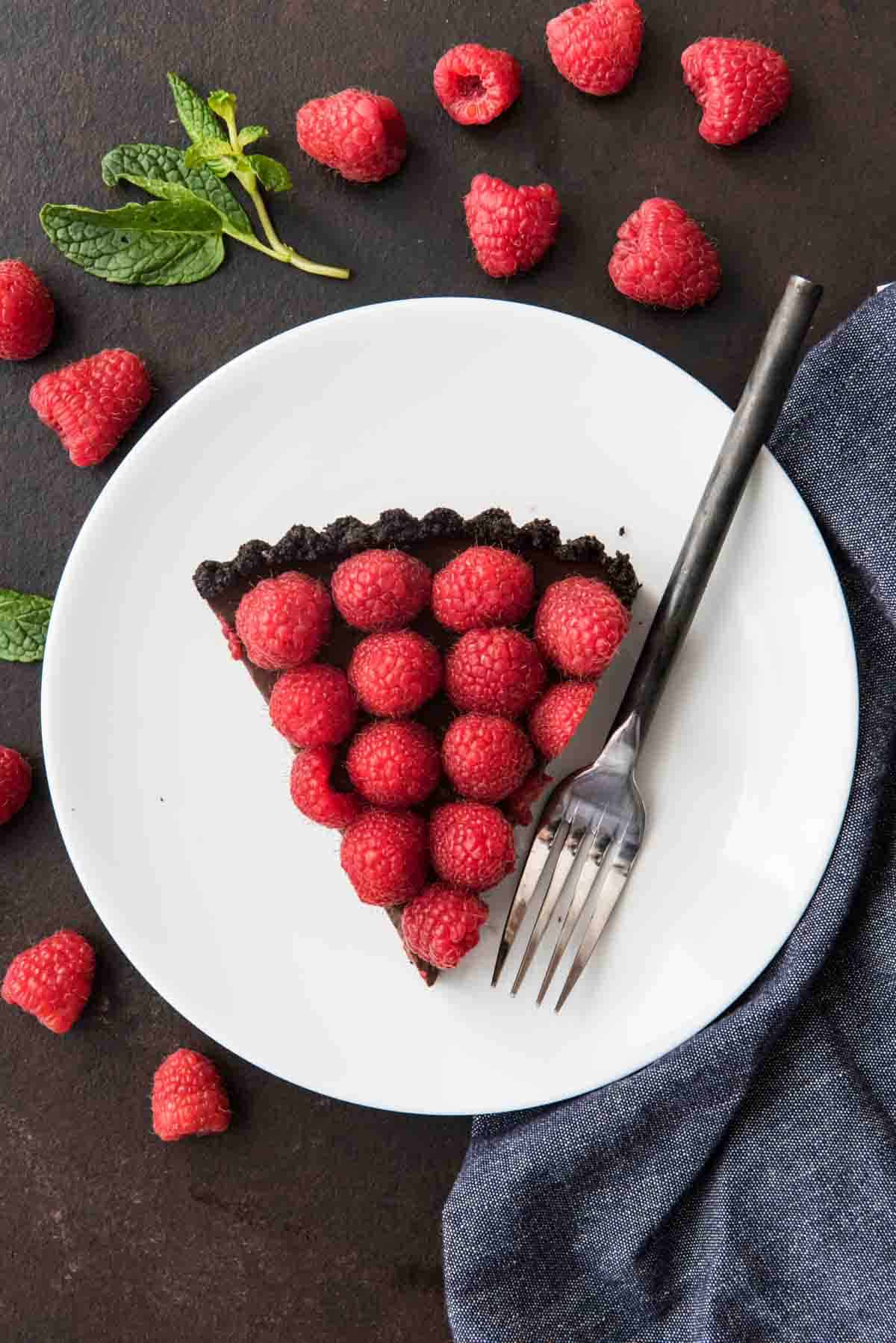 An overhead shot of a triangle slice of raspberry chocolate tart with a fork on a white plate. 