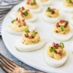 bacon and green onion deviled eggs on a serving platter with two forks to the side