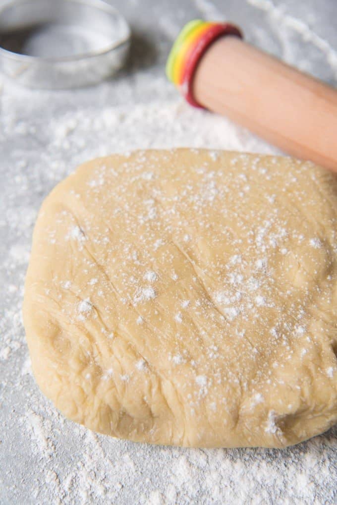 An image of a disc of chilled sugar cookie dough on a floured surface, ready to be rolled out and cut into shapes.