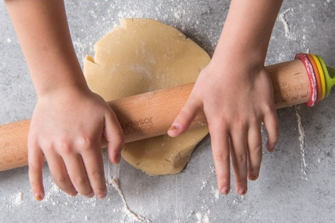 An image of hands on a rolling pin, rolling out sugar cookie dough.