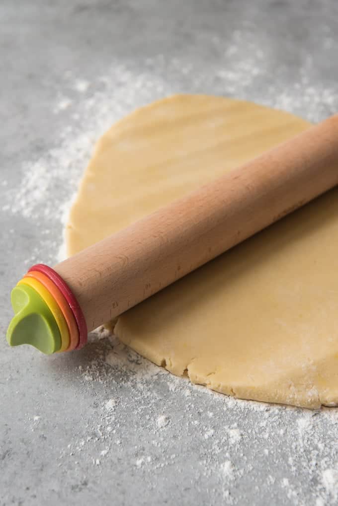 An image of a rolling pin resting on top of rolled out sugar cookie dough.