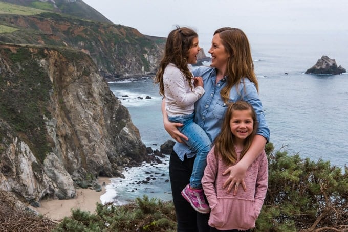 An image of a mother holding two daughters overlooking the sheer cliffs and ocean at Big Sur.
