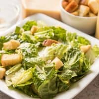 Homemade Caesar Salad in a square white bowl with croutons and cheese to the side
