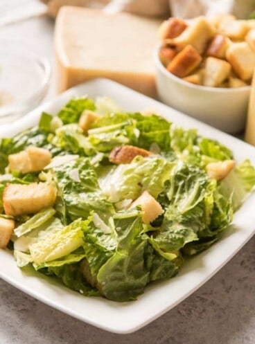 Homemade Caesar Salad in a square white bowl with croutons and cheese to the side