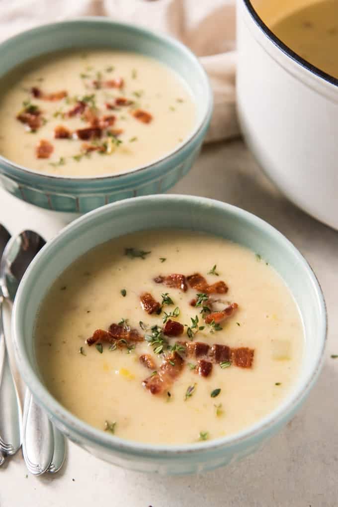 An image of two bowls of creamy potato leek soup, garnished with crispy crumbled bacon and thyme.