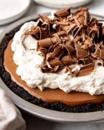 A homemade chocolate cream pie in a metal pan topped with whipped cream and chocolate curls.