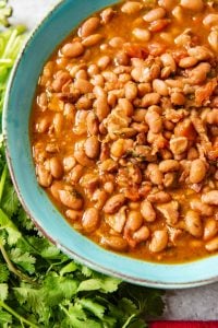 An image of a blue bowl full of charro beans (also known as frijoles charros or cowboy beans) made in a pressure cooker.