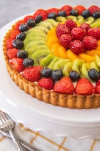 a fresh and colorful french fruit tart on a white cakestand