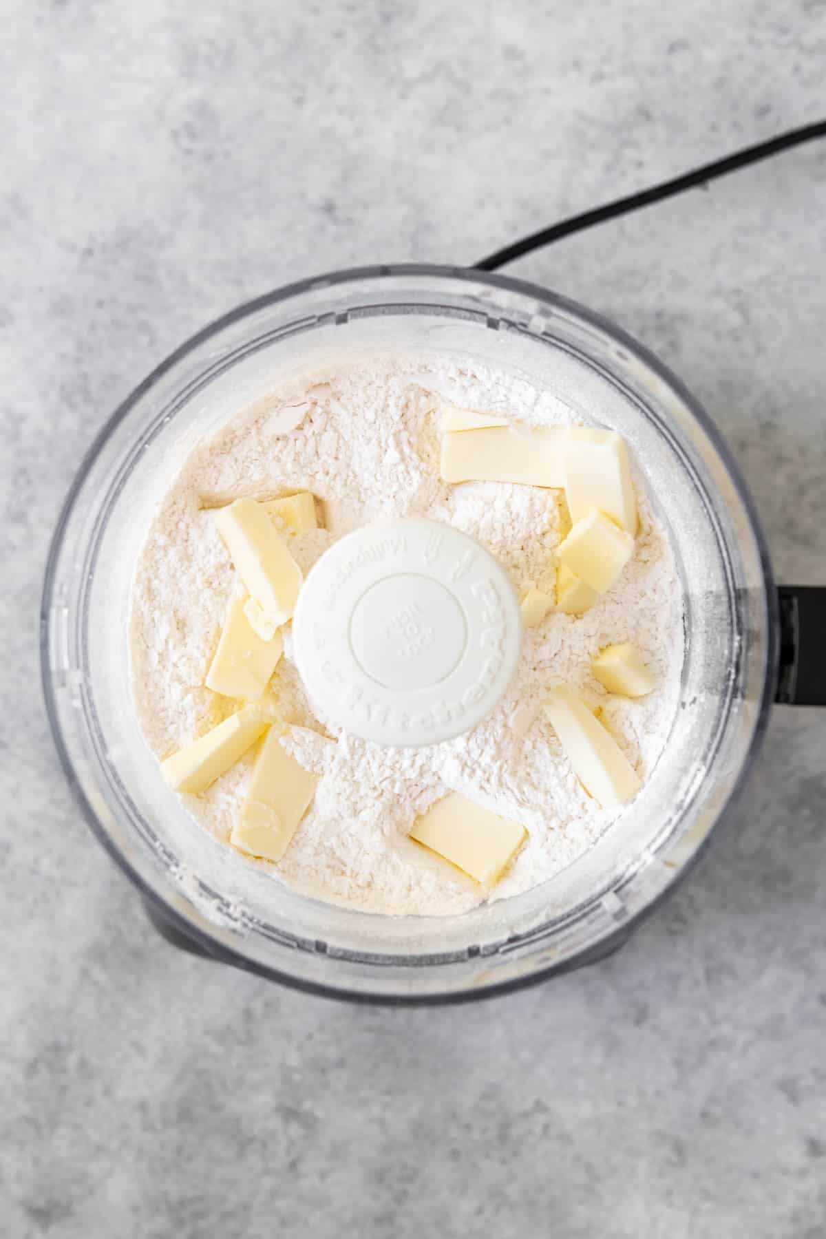 An image of cubed butter in the bowl of a food processor with flour and sugar for a sweet pastry crust for a French tart.