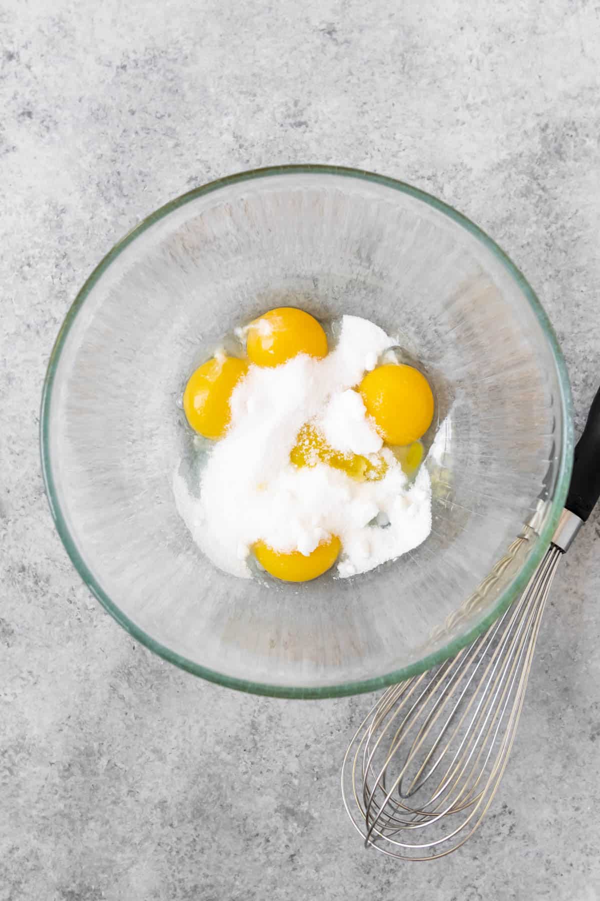 Egg yolks and sugar in a glass mixing bowl.