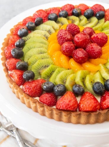 A fresh and colorful French fruit tart on a white cake stand.
