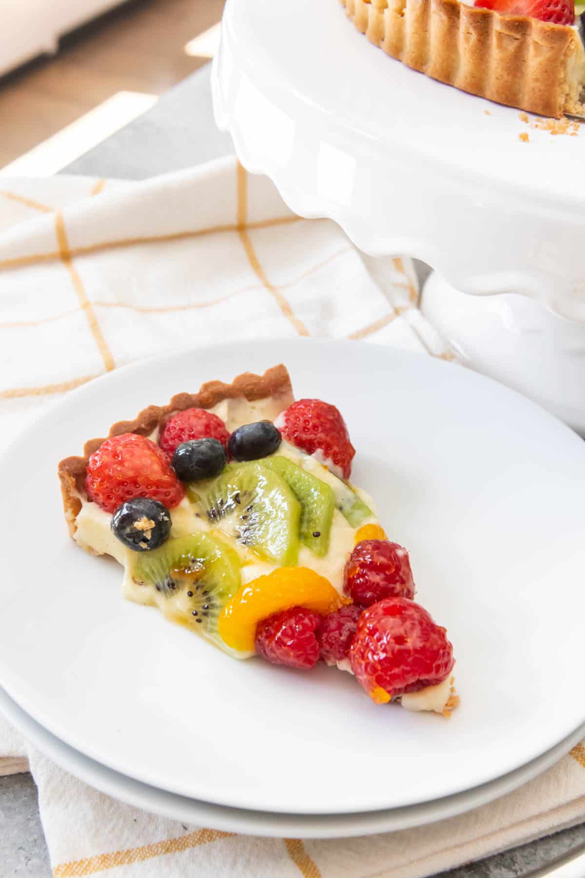 An image of a slice of mixed fruit tart made with pastry cream and a pate sucree sweet pastry crust.