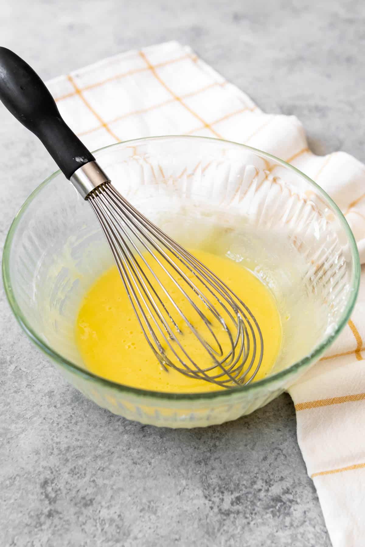 A whisk in a glass bowl filled with whisked egg yolks and sugar.
