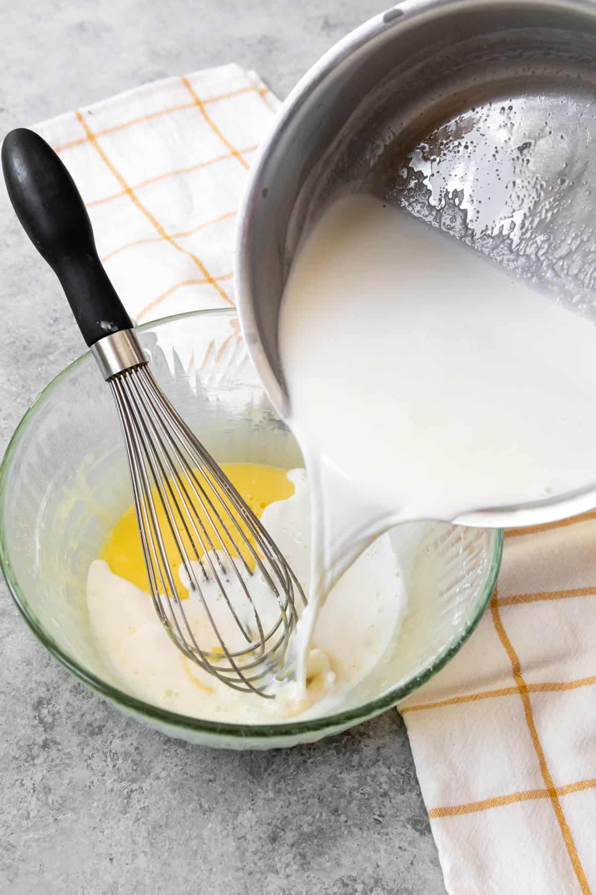 Adding hot milk to egg yolks in a glass bowl.