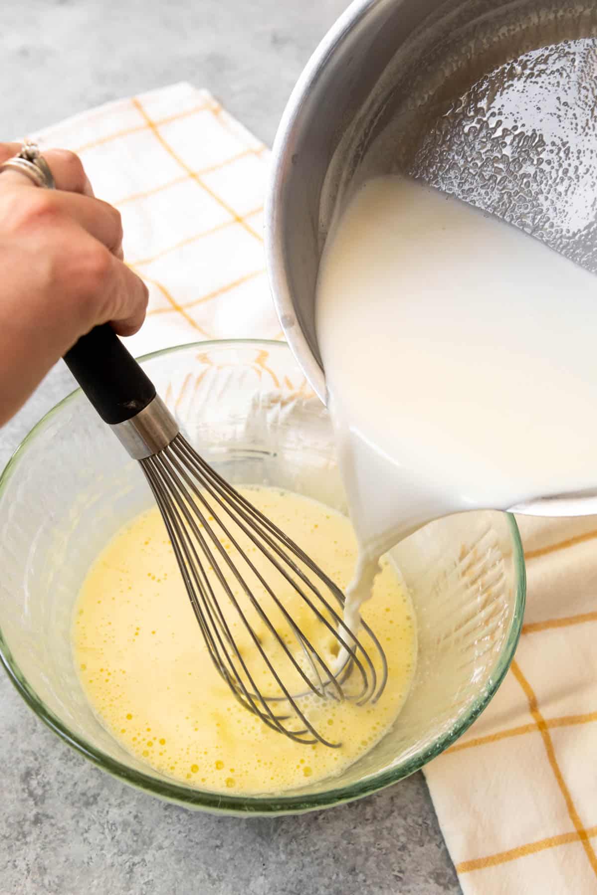 Tempering egg yolks and sugar by pouring hot milk into the whisked egg mixture while whisking so the yolks don't scramble.