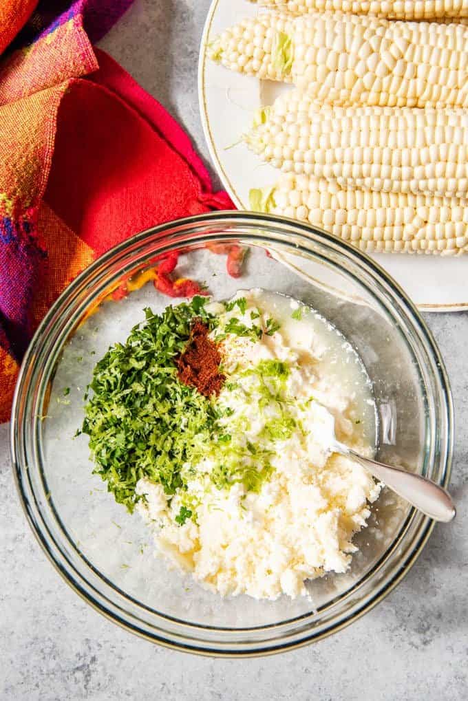 An image of a bowl with ingredients for making elotes - grilled Mexican street corn - a popular street food in Mexico and at food trucks in the United States.