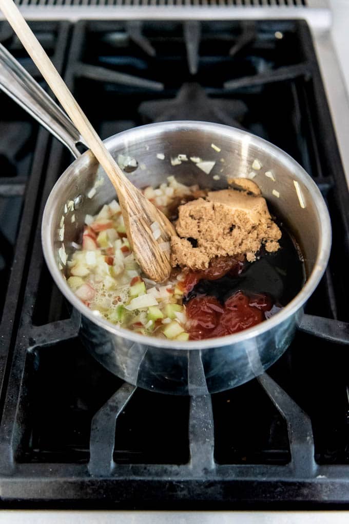 An image of a saucepan on the stovetop with chopped rhubarb, onion, brown sugar, molasses and other ingredients for homemade rhubarb bbq sauce.