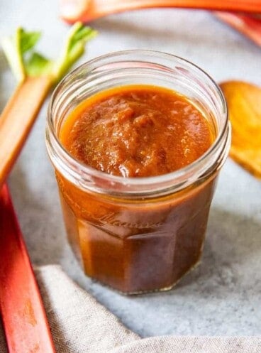 An image of a jar of homemade rhubarb barbecue sauce with stalks of rhubarb around it.