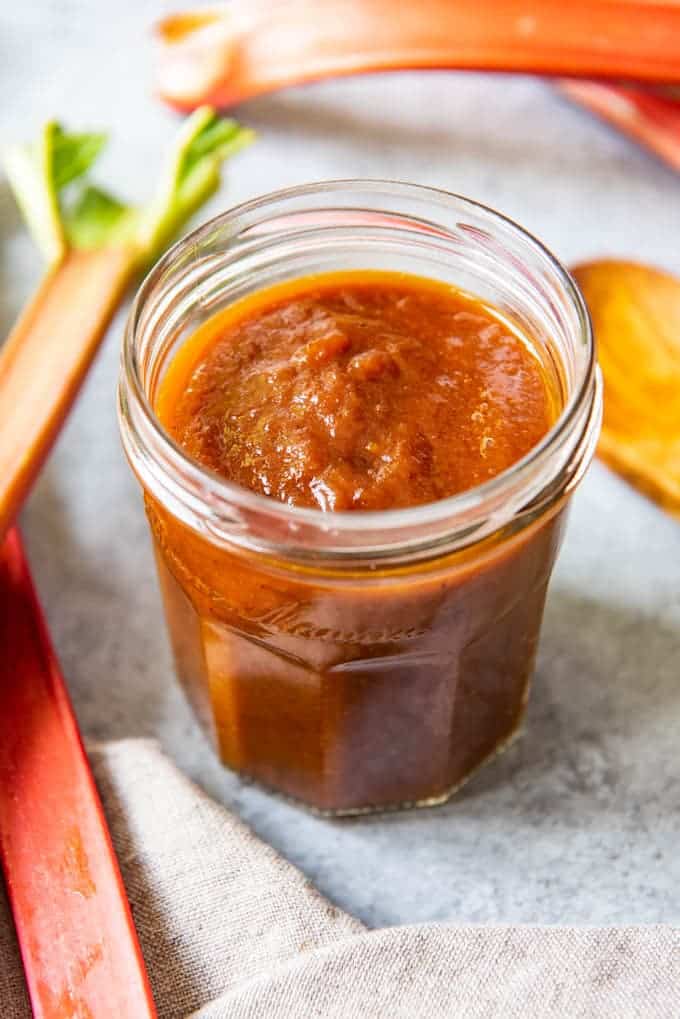 An image of a jar of homemade rhubarb barbecue sauce with stalks of rhubarb around it.