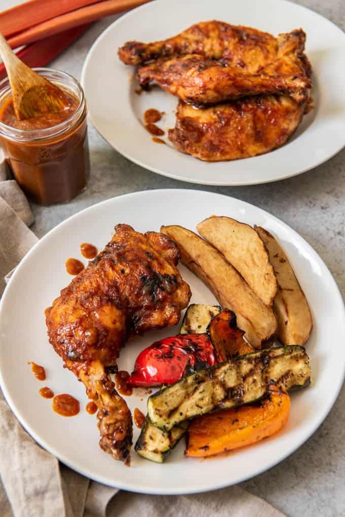 An image of a grilled chicken leg and thigh covered in homemade rhubarb bbq sauce with grilled vegetables and steak fries on the side.