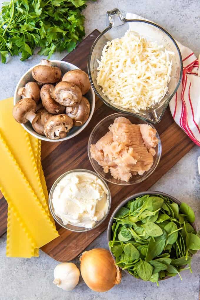 An image of the ingredients in bowls for a white chicken lasagna made with spinach and mushrooms.