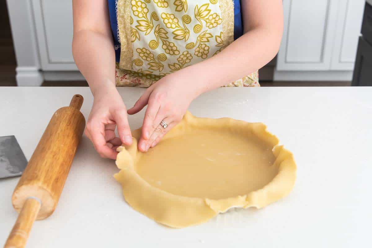 An image of hands pressing a sweet tart crust into a tart pan for a dessert tart.