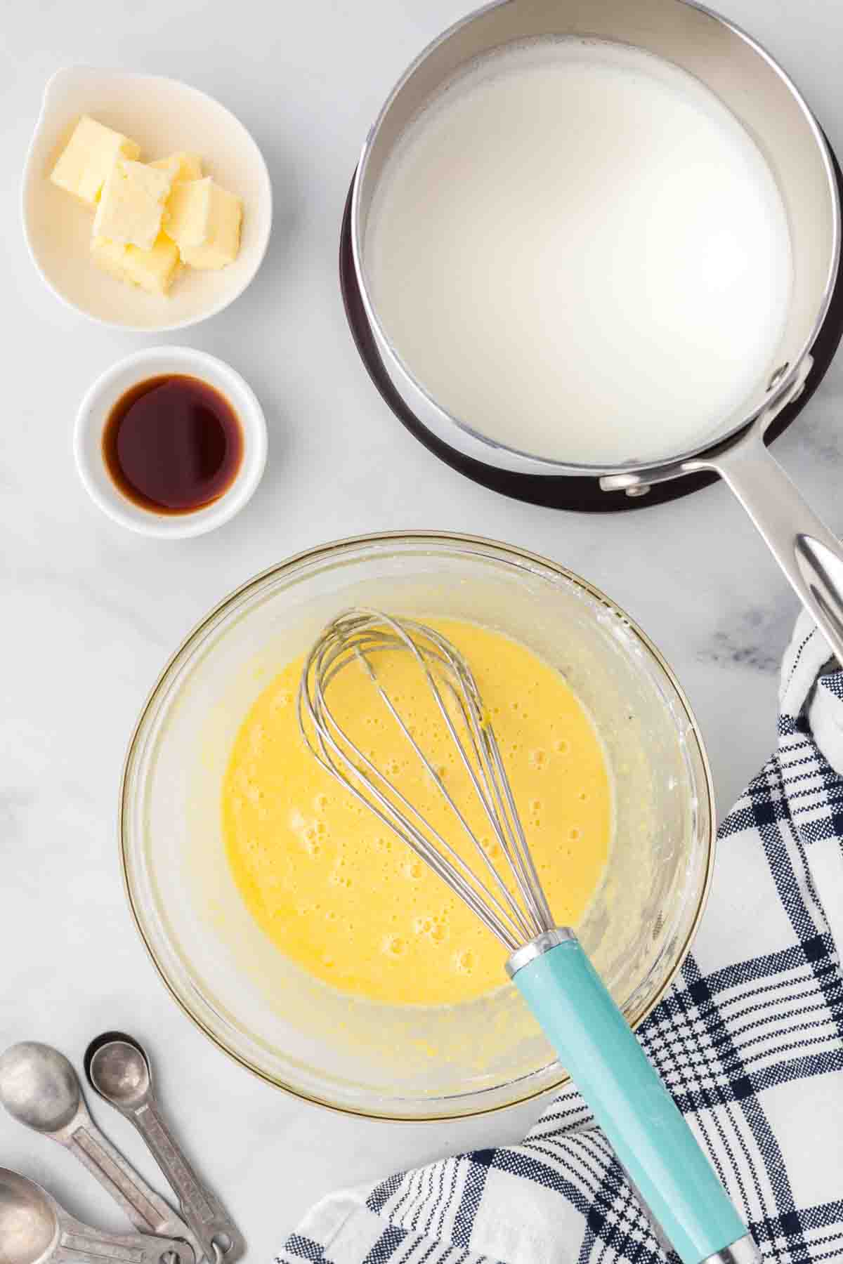 A whisk in a glass bowl filled with whisked egg yolks and sugar.